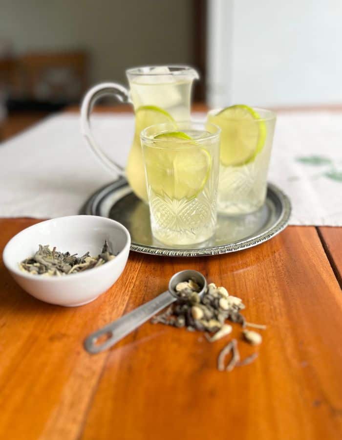 A tray with iced jasmine green tea in a pitcher, and two glasses. A bowl of loose-leaf jasmine green tea and a spoon.