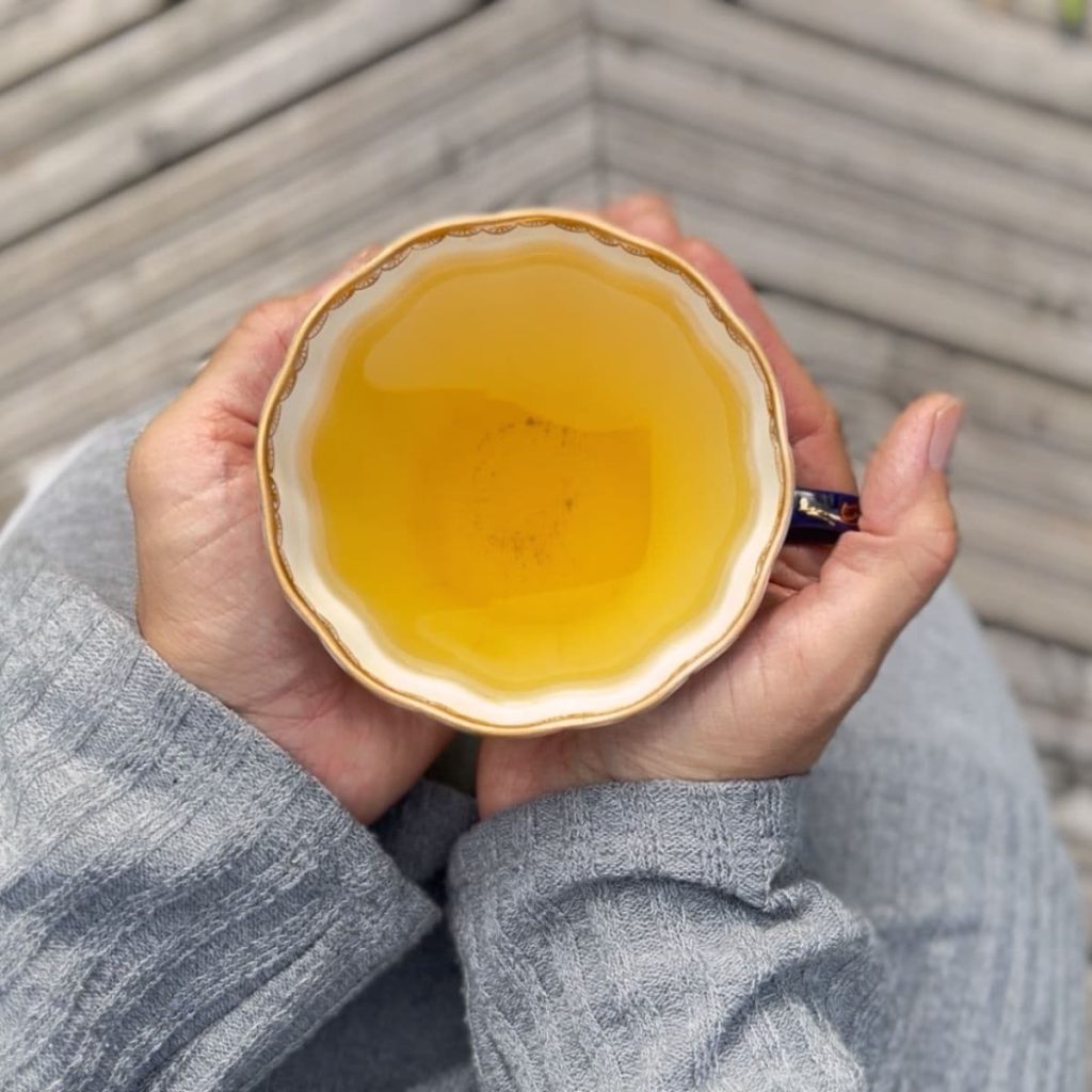A woman having her tea ritual and holding tea cup in her hands on a porch.