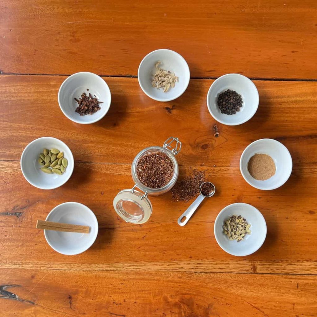Rooibos chai tea blend ingredients in tiny ceramic bowls around the rooibos tea jar.